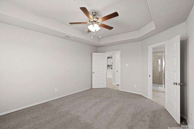 unfurnished bedroom featuring carpet flooring, ceiling fan, ensuite bathroom, and a tray ceiling