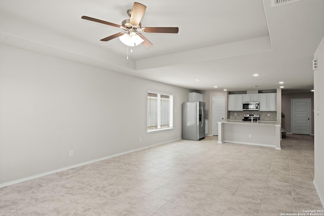 unfurnished living room featuring a raised ceiling and ceiling fan