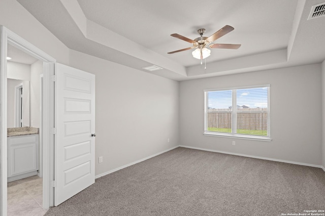 carpeted spare room with a tray ceiling and ceiling fan