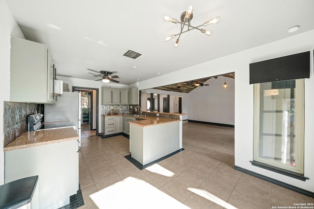 kitchen with sink, backsplash, kitchen peninsula, light tile patterned floors, and ceiling fan with notable chandelier