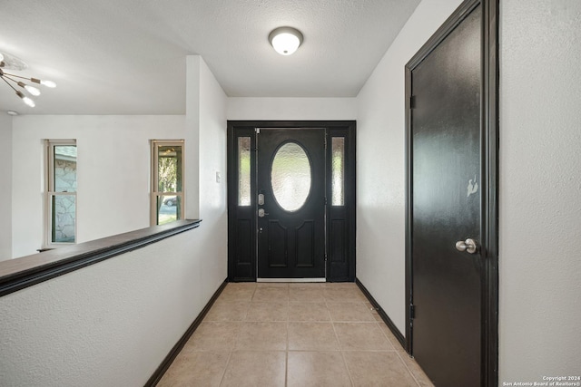 foyer featuring light tile patterned floors, a textured ceiling, and a chandelier