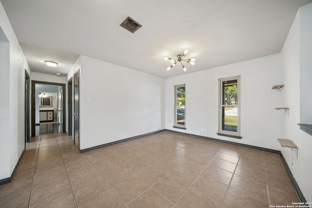 empty room with light tile patterned floors, a textured ceiling, and an inviting chandelier