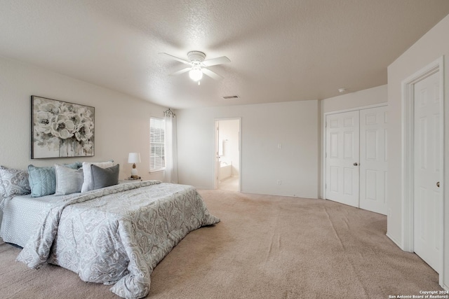 bedroom with ensuite bath, a textured ceiling, light colored carpet, ceiling fan, and a closet