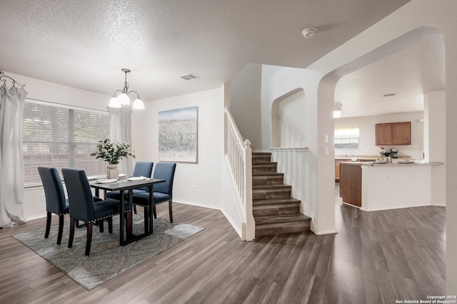 dining room featuring dark wood-type flooring, a textured ceiling, and an inviting chandelier