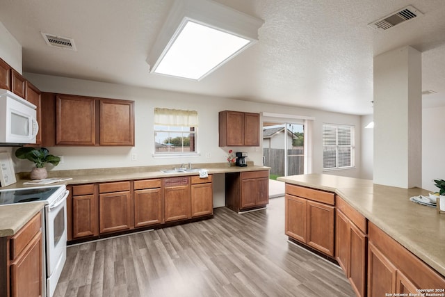 kitchen featuring white appliances, sink, light wood-type flooring, a textured ceiling, and kitchen peninsula