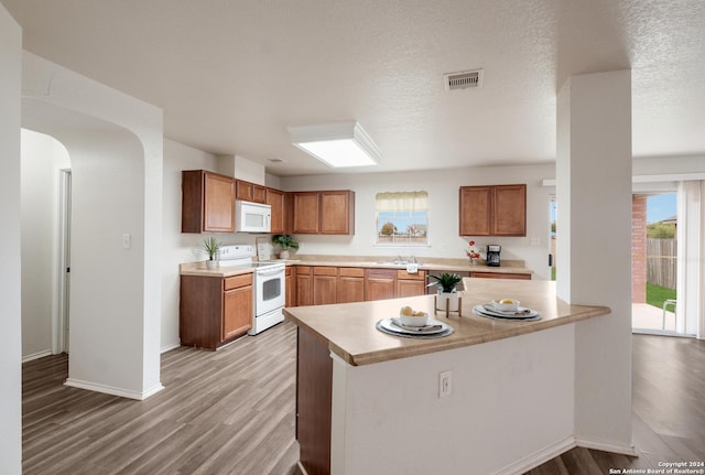 kitchen featuring sink, light hardwood / wood-style flooring, kitchen peninsula, a textured ceiling, and white appliances