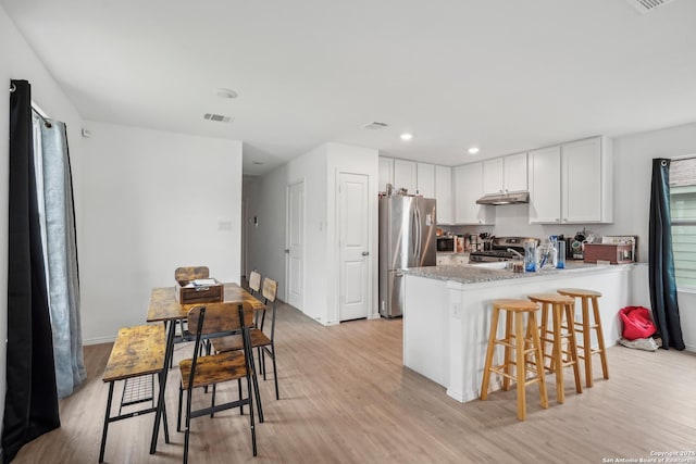 kitchen featuring white cabinets, appliances with stainless steel finishes, light hardwood / wood-style flooring, and a breakfast bar area