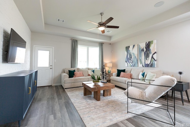 living room with hardwood / wood-style floors, a raised ceiling, and ceiling fan