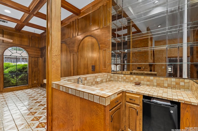 kitchen featuring backsplash, coffered ceiling, wooden walls, tile counters, and beam ceiling