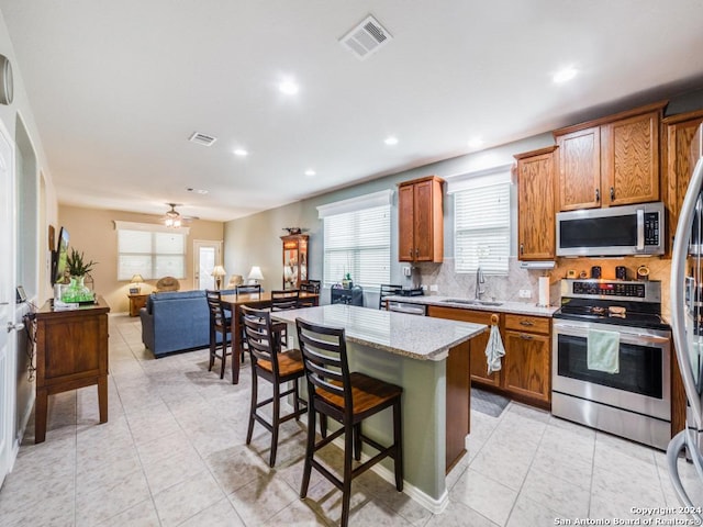 kitchen with ceiling fan, sink, a center island, a kitchen breakfast bar, and appliances with stainless steel finishes