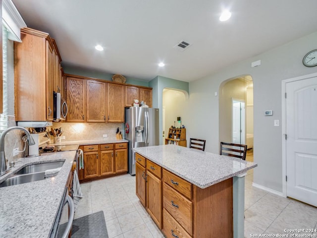 kitchen featuring sink, tasteful backsplash, a kitchen island, light stone counters, and stainless steel appliances