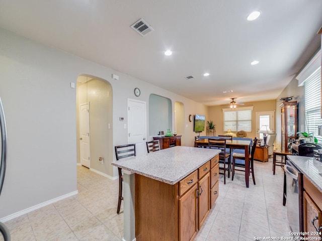 kitchen with light stone countertops, ceiling fan, a center island, stainless steel dishwasher, and light tile patterned floors