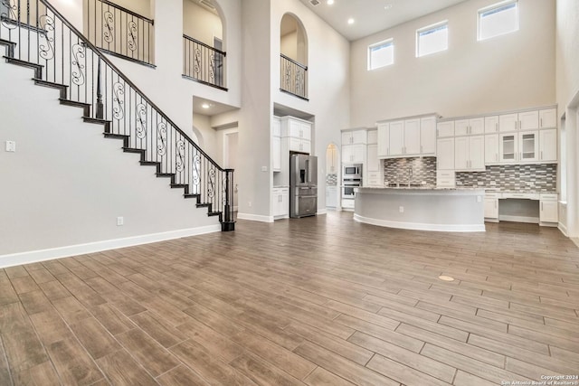 unfurnished living room featuring light wood-type flooring and a towering ceiling