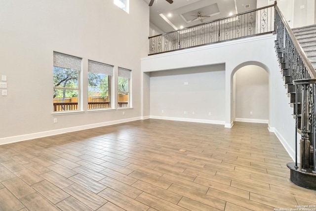 unfurnished living room featuring a towering ceiling, light hardwood / wood-style floors, and ceiling fan