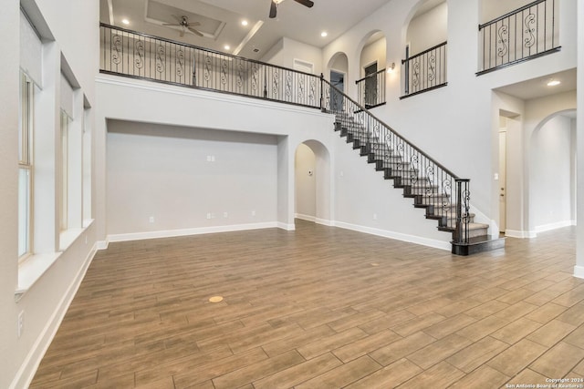 unfurnished living room featuring wood-type flooring, a towering ceiling, and ceiling fan