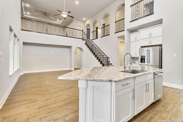 kitchen featuring white cabinetry, a towering ceiling, a kitchen island with sink, and appliances with stainless steel finishes