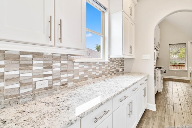 kitchen featuring white cabinets, stainless steel range with gas cooktop, tasteful backsplash, light hardwood / wood-style floors, and light stone counters