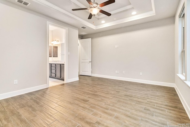 empty room with ceiling fan, light hardwood / wood-style floors, a raised ceiling, and ornamental molding