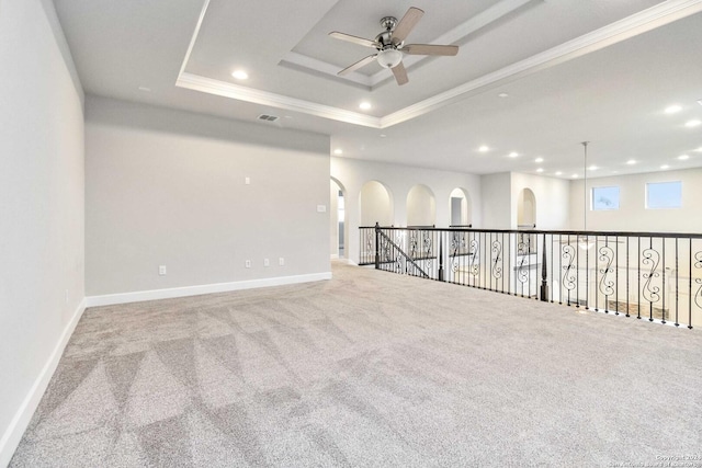 carpeted empty room featuring a raised ceiling, crown molding, and ceiling fan