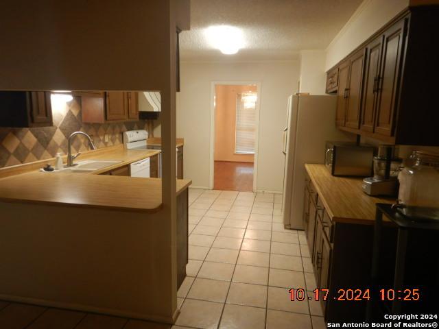 kitchen with kitchen peninsula, backsplash, white appliances, sink, and light tile patterned flooring