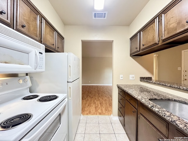 kitchen featuring dark brown cabinetry, sink, light hardwood / wood-style flooring, dark stone counters, and white appliances