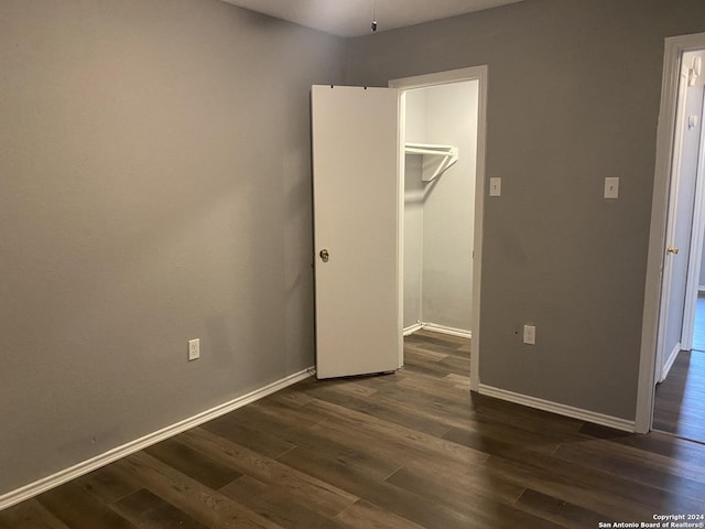 unfurnished bedroom featuring a walk in closet, a closet, and dark wood-type flooring