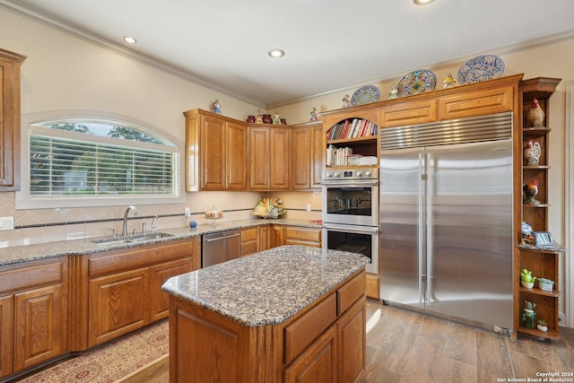 kitchen featuring sink, stainless steel appliances, ornamental molding, a kitchen island, and light wood-type flooring