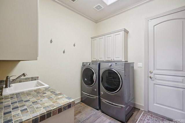 clothes washing area with cabinets, crown molding, sink, independent washer and dryer, and wood-type flooring