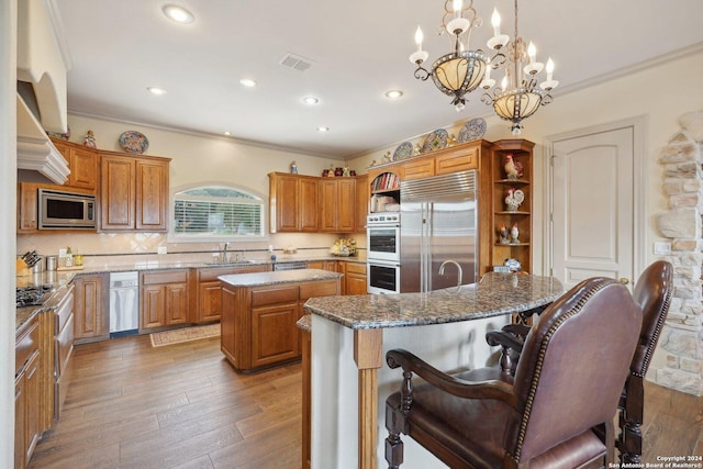 kitchen with sink, hanging light fixtures, dark wood-type flooring, built in appliances, and a kitchen island