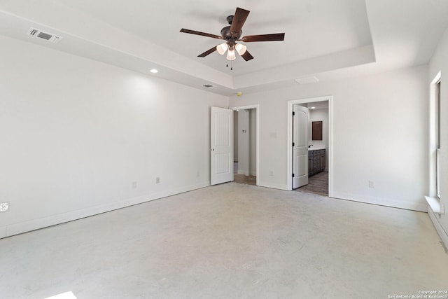 unfurnished bedroom featuring a tray ceiling, connected bathroom, and ceiling fan