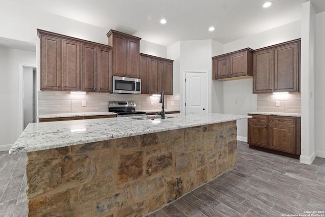 kitchen featuring light stone countertops, appliances with stainless steel finishes, tasteful backsplash, a kitchen island with sink, and sink