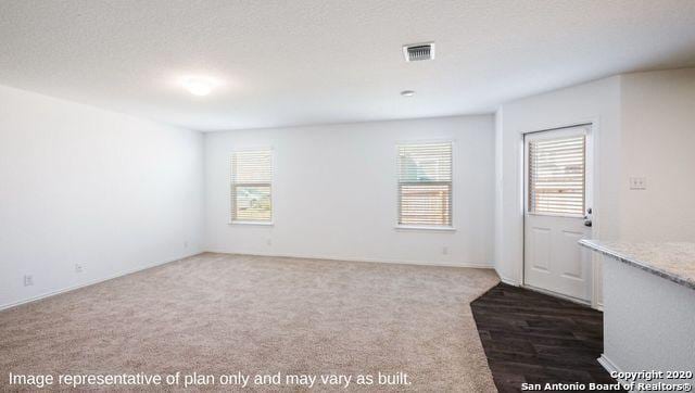 empty room featuring a healthy amount of sunlight, a textured ceiling, and dark colored carpet