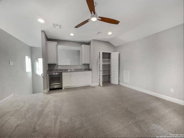 unfurnished living room with wine cooler, light carpet, and vaulted ceiling