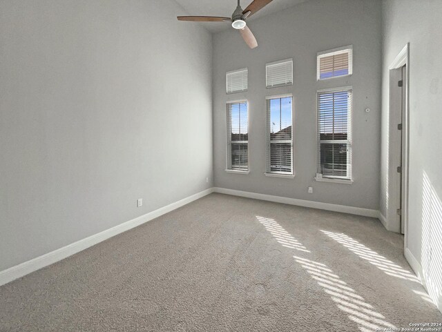 carpeted spare room with ceiling fan and a towering ceiling