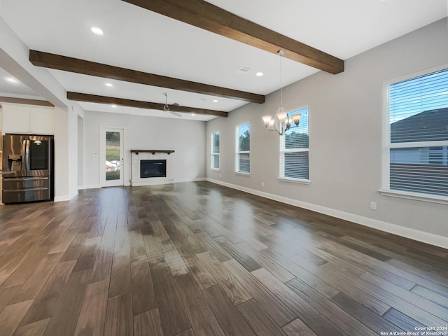 unfurnished living room featuring beam ceiling, dark hardwood / wood-style flooring, a healthy amount of sunlight, and a notable chandelier