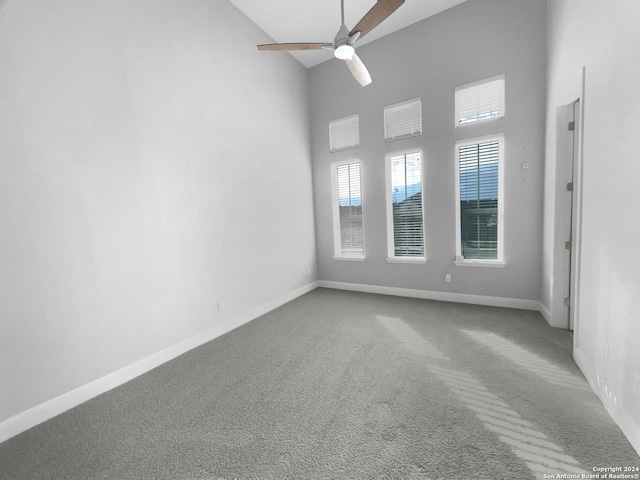 carpeted empty room with high vaulted ceiling and ceiling fan