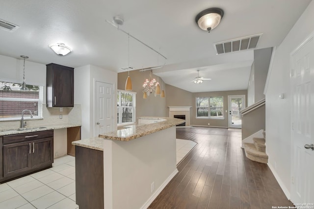 kitchen featuring lofted ceiling, ceiling fan with notable chandelier, sink, light wood-type flooring, and a kitchen island