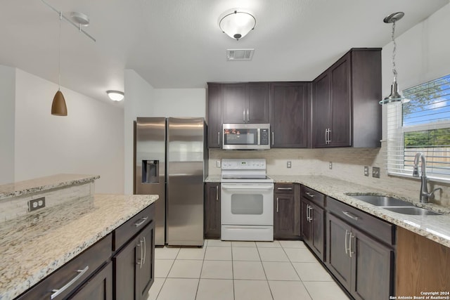 kitchen featuring light stone counters, sink, stainless steel appliances, and decorative light fixtures