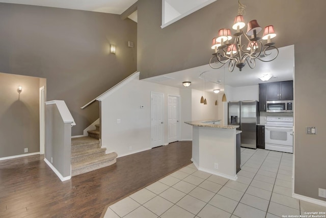 kitchen with light stone countertops, appliances with stainless steel finishes, light wood-type flooring, an inviting chandelier, and high vaulted ceiling