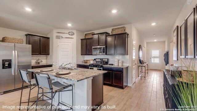 kitchen with decorative backsplash, light wood-type flooring, stainless steel appliances, and an island with sink