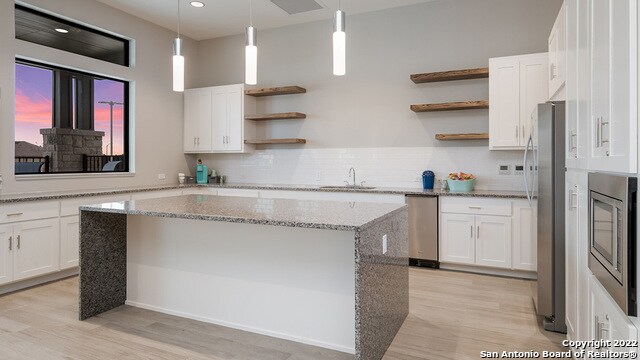 kitchen featuring sink, light stone countertops, a kitchen island, white cabinetry, and stainless steel appliances