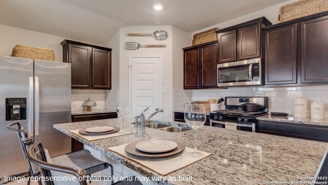 kitchen with sink, appliances with stainless steel finishes, tasteful backsplash, dark brown cabinets, and light stone counters