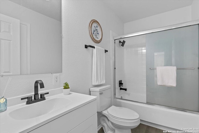 full bathroom with combined bath / shower with glass door, hardwood / wood-style floors, vanity, and toilet