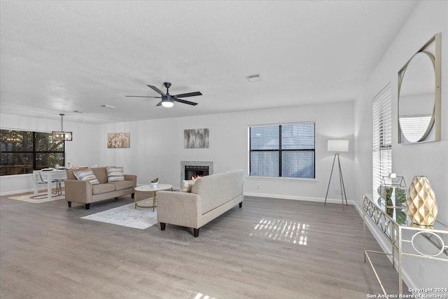 living room with ceiling fan, a healthy amount of sunlight, light wood-type flooring, and a fireplace