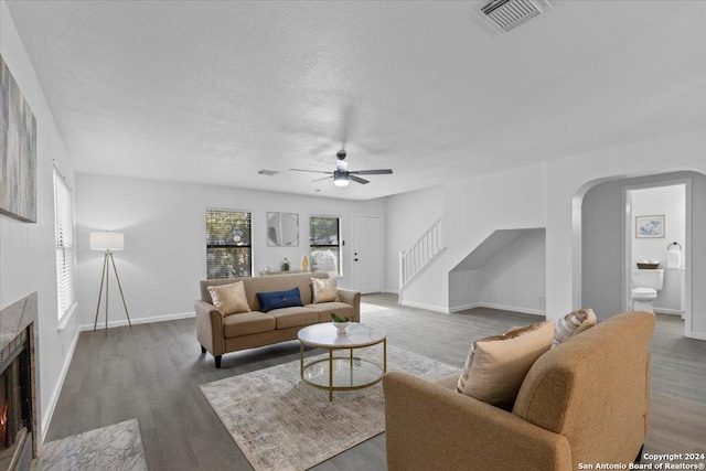 living room with a textured ceiling, ceiling fan, and dark wood-type flooring