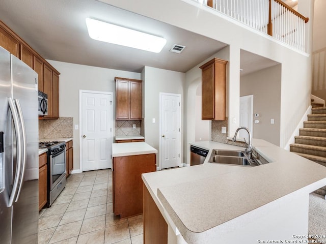 kitchen featuring kitchen peninsula, backsplash, stainless steel appliances, sink, and a center island