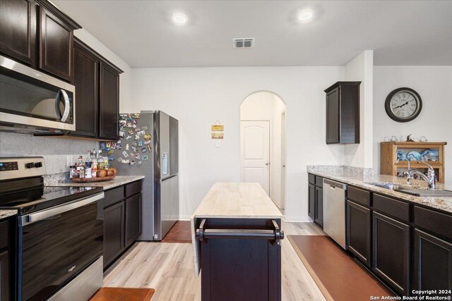 kitchen featuring light stone countertops, sink, a center island, stainless steel appliances, and light wood-type flooring