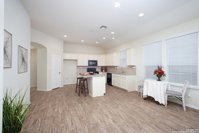 kitchen with a breakfast bar, white cabinetry, a kitchen island, and black appliances