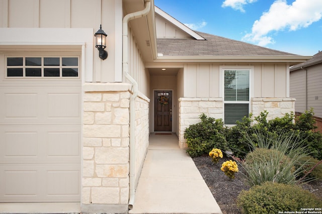 property entrance with a garage, stone siding, a shingled roof, and board and batten siding