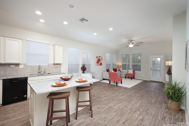 kitchen with a kitchen breakfast bar, a center island, light hardwood / wood-style flooring, black dishwasher, and white cabinetry